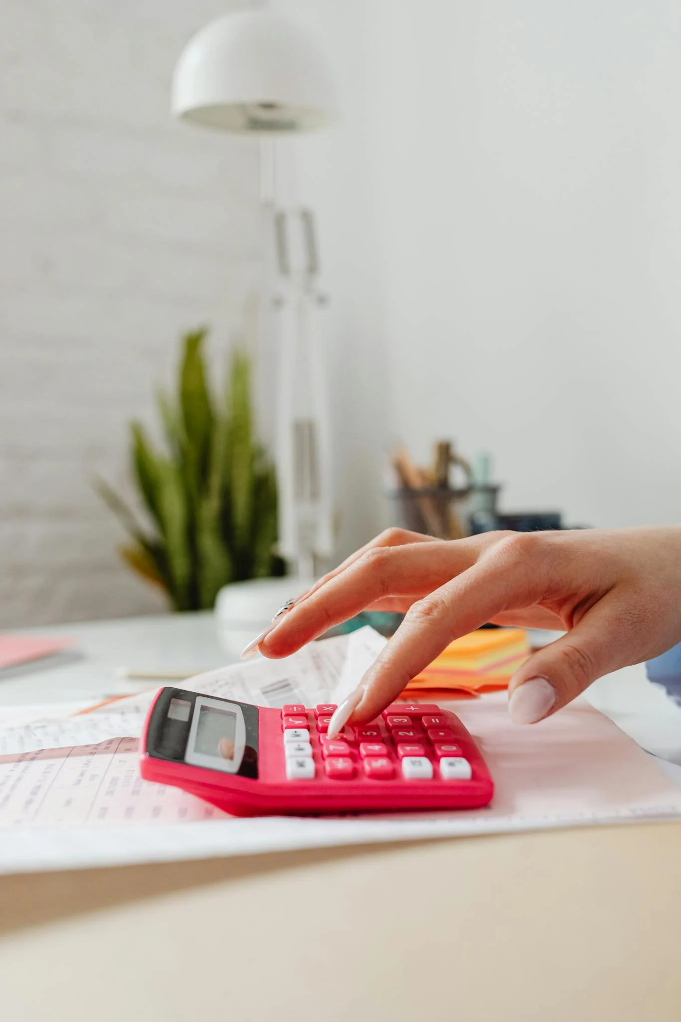 Close-up of a hand pressing buttons on a pink calculator on a desk, indoors.